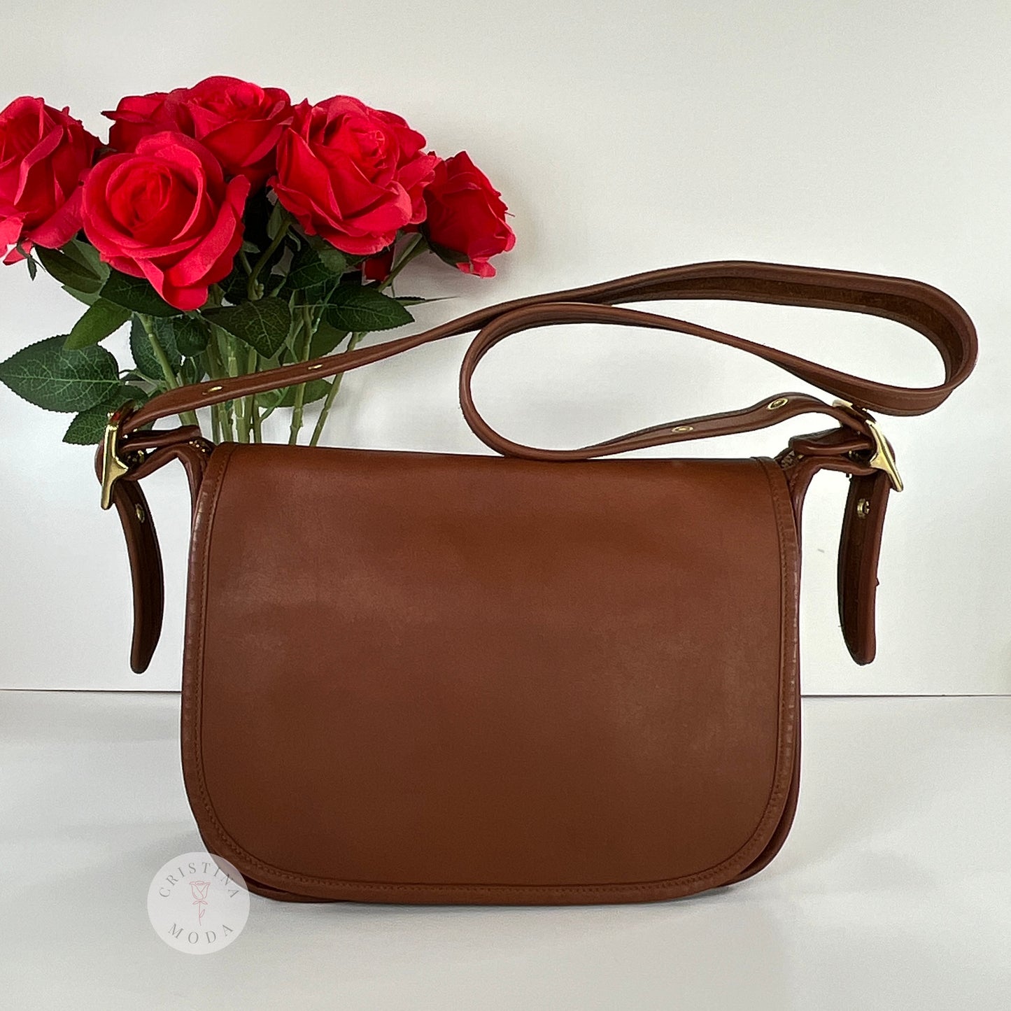 View of front of vintage coach Patricia's Legacy Bag in British Tan in front of white backdrop and vase of roses in background