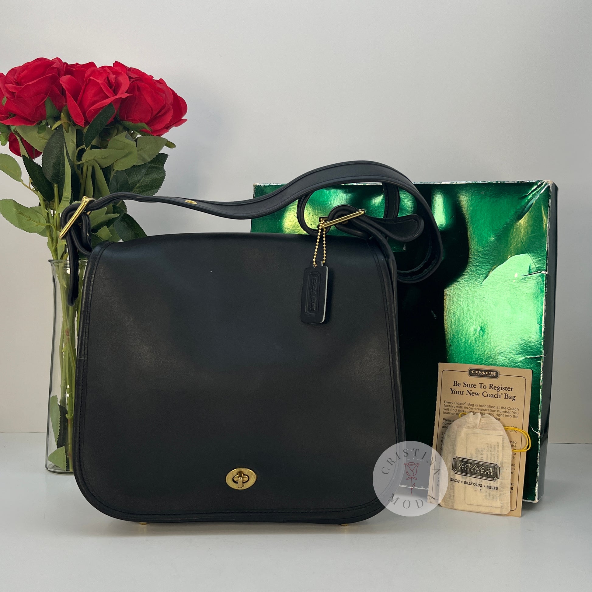 The cover shot of the vintage coach stewardess bag- the bag in front of the box and paperwork it comes with, with a bouquet of roses in the background